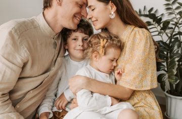A loving family of four shares a tender moment in a cozy indoor setting, embracing and smiling.