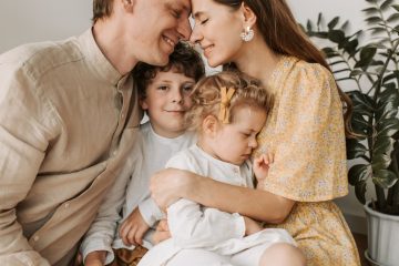 A loving family of four shares a tender moment in a cozy indoor setting, embracing and smiling.