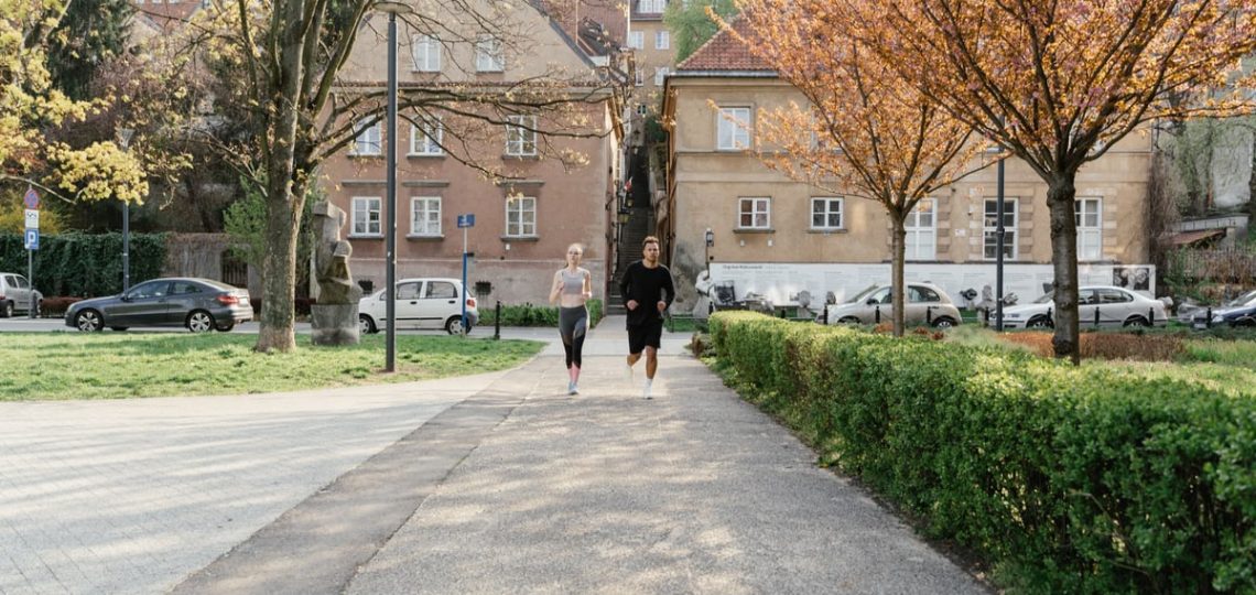 A couple jogging together in an urban park surrounded by greenery and houses.