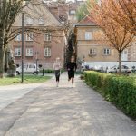 A couple jogging together in an urban park surrounded by greenery and houses.