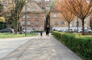 A couple jogging together in an urban park surrounded by greenery and houses.