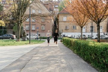 A couple jogging together in an urban park surrounded by greenery and houses.