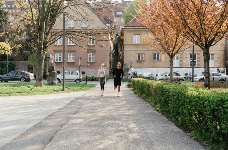 A couple jogging together in an urban park surrounded by greenery and houses.