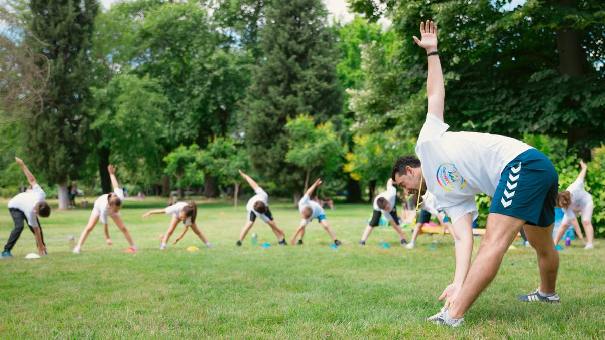 Kids stretching exercises in a park guided by a coach, promoting fitness and fun.